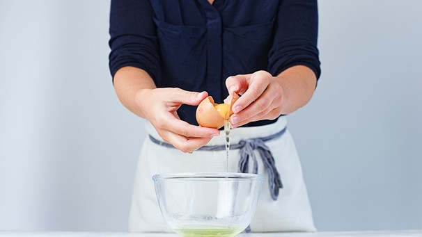 Frau schlägt ein Ei über einer Schüssel auf | Bild: mauritius images / foodcollection / Charlie Richards