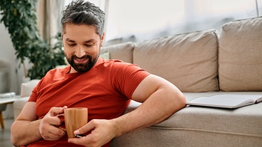 Mann trinkt zu Hause eine Tasse Kaffee mit Pflanzenmilch. | Bild: mauritius images / LightField Studios Inc. / Alamy / Alamy Stock Fotos