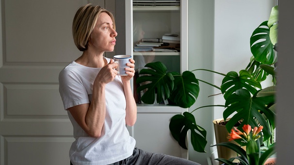 Eine Frau trinkt Kaffee aus einer Tasse und sieht aus dem Fenster | Bild: mauritius images / Dmitry Marchenko / Alamy / Alamy Stock Fotos