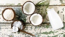 Verschiedene Kokosprodukte wie Kokosflocken, Kokosmilch und Kokosöl in Kokosschalen auf einer Holzunterlage | Bild: mauritius images / The Picture Pantry / Natasha Breen