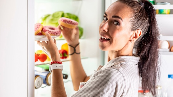 Eine Frau öffnet ihren Kühlschrank, um sich einen Donut zu holen | Bild: mauritius images / Weyo / Alamy / Alamy Stock Photos