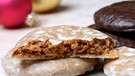 Ein geteilter, mit Zuckerguss glasierter Oblatenlebkuchen liegt auf einem anderen, daneben Schokolebkuchen. Im Hintergrund Christbaumkugeln. | Bild: picture alliance / imageBROKER | J. Pfeiffer