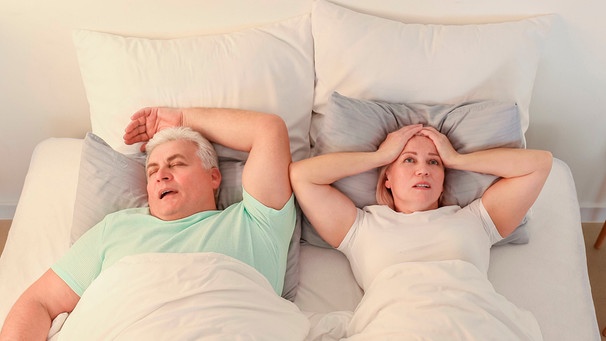 Frau liegt verzweifelt und schlaflos in einem Doppelbett neben einem Mann, der schnarcht | Bild: mauritius Bilder / Pixel-shot / Alamy / Alamy Stock Fotos