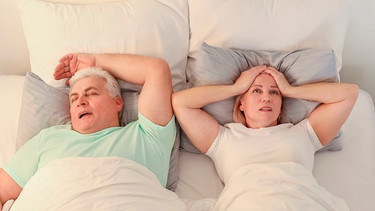 Frau liegt verzweifelt und schlaflos in einem Doppelbett neben einem Mann, der schnarcht | Bild: mauritius Bilder / Pixel-shot / Alamy / Alamy Stock Fotos