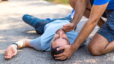 Ein mobiler Retter kniet neben einem Mann nach einem Unfall und leistet Erste Hilfe. | Bild: mauritius Bilder / Bymandesigns / Alamy / Alamy Stock Fotos