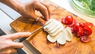 Frau schneidet Mozzarella auf einem Holzbrett | Bild: mauritius images / Westend61 RF / Anke Scheibe