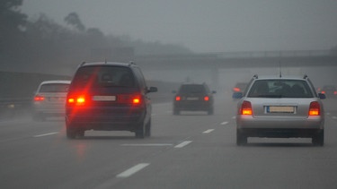 Mehrere Fahrzeuge fahren bei Nebel auf einer Autobahn mit angeschalteter Nebelschlussleuchte. | Bild: mauritius images / Blickwinkel / Alamy / Alamy Stock Fotos