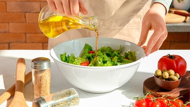 Frau bereitet einen Salat mit Olivenöl zu. | Bild: mauritius images / Pixel-shot / Alamy / Alamy Stock Photos