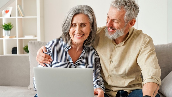 Ein fröhliches Paar mittleren Alters sitzt auf einer Couch mit einem Laptop und shoppt online | Bild: mauritius Bilder / Insta_photos / Alamy / Alamy Stock Fotos