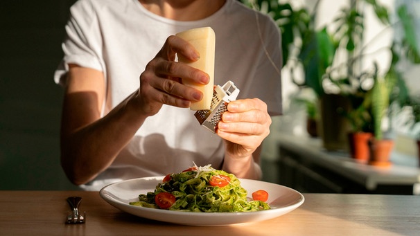 Frau reibt parmesan über die Pasta mit Pesto | Bild: mauritius images / Dmitry Marchenko / Alamy / Alamy Stock Photos