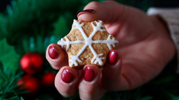 Frau hält ein Weihnachtsplätzchen in der Hand, das mit Zuckerguss verziert ist | Bild: mauritius images / Emilija Randjelovic / Alamy / Alamy Stock Photos