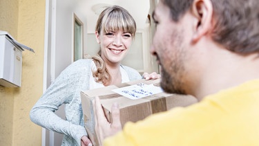 Paketbote übergibt einer Frau ein Paket an der Wohnungstür | Bild: mauritius images / Westend61 / Jo Kirchherr