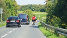 Zwei Pkw überholen auf einer Landstraße zwei Radfahrer sehr knapp | Bild: mauritius images / Pitopia / XXLPhoto