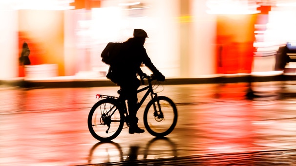 Radfahrer fährt nachts in der Stadt an beleuchteten Schaufenstern vorbei | Bild: mauritius images / Christian Müller / Alamy / Alamy Stock Photos