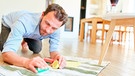 Ein Mann bearbeitet einen Rotweinfleck auf einem Teppich mit Salz | Bild: mauritius images / Robert Kneschke / Alamy / Alamy Stock Photos