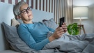 Frau liegt im Bett und schaut kritisch auf ihr Smartphone | Bild: mauritius images / Science Photo Library / Microgen Images