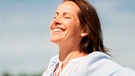 Frau steht an einem Geländer und hält ihr Gesicht mit geschlossenen Augen in die Sonne. | Bild: mauritius images / Lev Dolgachov / Alamy / Alamy Stock Photos