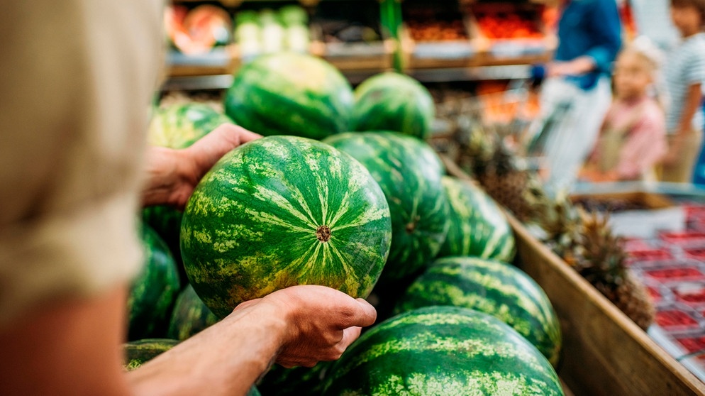 Ein Arm greift in einem Supermarkt nach einer Wassermelone | Bild: mauritius images / LightField Studios Inc. / Alamy / Alamy Stock Photos