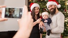 Ein Handybild wird zu Weihnachten vor dem Christbaum von einer jungen Familie gemacht gemacht | Bild: mauritius images / Cavan images / Dreet Production