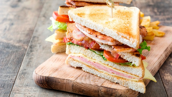 Auf einem Holzbrett liegt ein saftig belegtes Clubsandwich. | Bild: mauritius images / David Cabrera Navarro / Alamy / Alamy Stock Photos