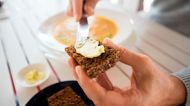 Mann bestreicht eine Scheibe Brot mit Butter | Bild: mauritius images / Lev Dolgachov / Alamy / Alamy Stock Photos