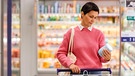 Frau schaut im Supermarkt skeptisch auf eine Lebensmittelverpackung | Bild: mauritius images / SeventyFour Images / Alamy / Alamy Stock Photos