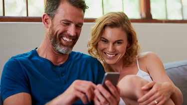 Eine Frau hält eine Tasse Tee und blickt zufrieden in ihr Smartphone. | Bild: mauritius images / Yuri Arcurs / Alamy / Alamy Stock Photos