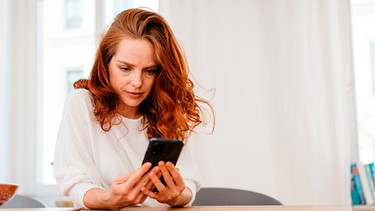 Eine Frau sieht nachdenklich auf ihr Handy | Bild: mauritius images / Ralf Cornesse / Alamy / Alamy Stock Photos