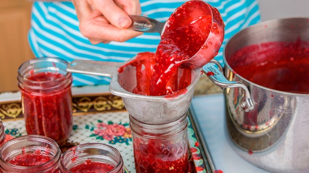 Eine Frau, man sieht nur ihre Hände, gießt frisch eingekochte Marmelade über einen Trichter in ein Glas | Bild: mauritius images / Janet Horton / Alamy / Alamy Stock Photos