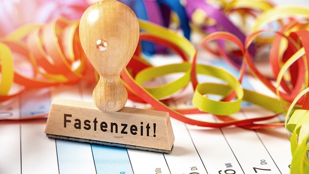 Auf einem Kalender liegen Luftschlangen, die das Ende der Faschingszeit symbolisieren und ein Stempel mit dem Aufdruck "Fastenzeit". | Bild: mauritius images / Chromorange / Michael Bihlmayer