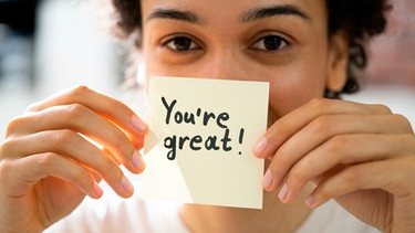 Frau hält Haftnotiz in der Hand, auf der steht "You're great" | Bild: mauritius images / Andriy Popov / Alamy / Alamy Stock Photos