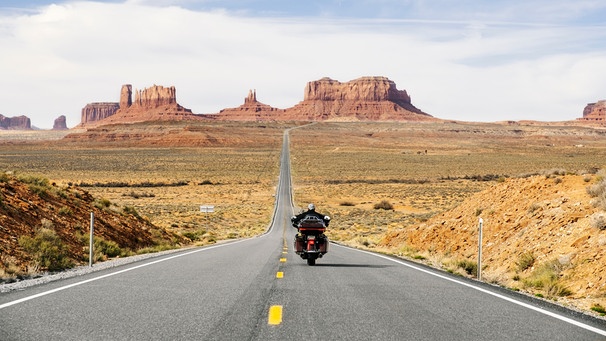 Rückansicht eines Motorradfahrers, der eine Straße im Monument Valley Tribal Park in Utah entlangfährt  | Bild: mauritius images / Westend61 / Daniel González
