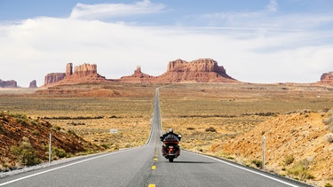 Rückansicht eines Motorradfahrers, der eine Straße im Monument Valley Tribal Park in Utah entlangfährt  | Bild: mauritius images / Westend61 / Daniel González