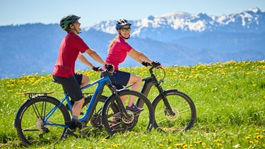 Ein Paar fährt mit den E-Bikes bei Penzberg über einen Feldweg | Bild: mauritius images / Jan Greune