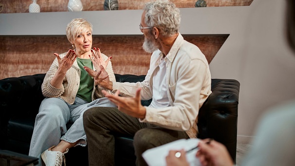 Ein Paar mittleren Alters sitzt auf der Couch, unterhält sich und gestikuliert dabei.  | Bild: mauritius images / LightField Studios Inc. / Alamy / Alamy Stock Photos