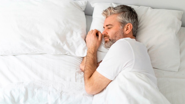 Ein Mann mit graumelierten Haaren schläft im Bett | Bild: mauritius images / Prostock-studio / Alamy / Alamy Stock Photos