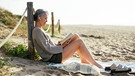 Eine Frau liest ein Buch am Strand | Bild: mauritius images/ Westend61 RF
