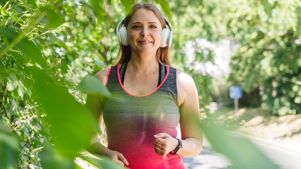 Frau joggt mir Kopfhörern durch einen Park | Bild: mauritius images  Westend61  Ok Shu