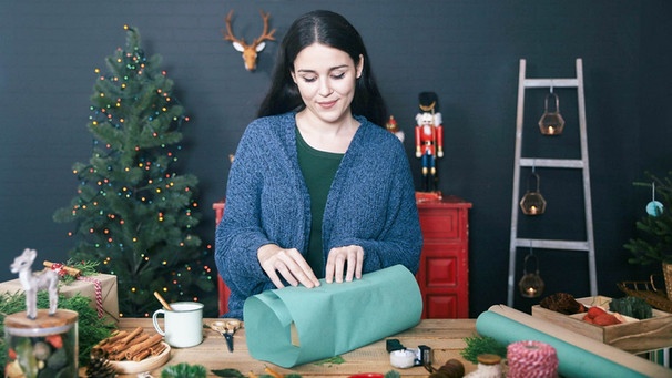 Frau verpackt ein Weihnachtspäckchen | Bild: mauritius images / Westend61 / Retales Botijero