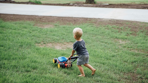 Ein kleiner Junge mäht mit einem Spielzeug den Rasen | Bild: mauritius images / Cavan Images / Kimberli Fredericks