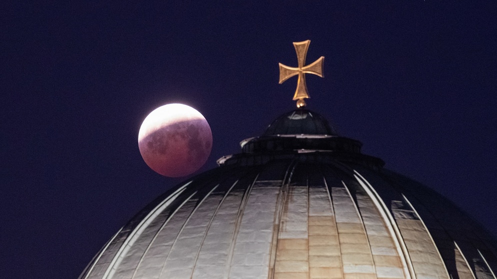 21.01.2019, Bayern, Nürnberg: Als roter, sogenannter «Blutmond» steht der Vollmond über der Kuppel der Kirche St. Elisabeth, während er aus dem Kernschatten der Erde tritt. Foto: Daniel Karmann/dpa +++ dpa-Bildfunk +++ | Bild: dpa-Bildfunk/Daniel Karmann