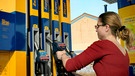 Frau zieht an einer Tankstelle die den Zapfhahn aus der Säule. | Bild: mauritius images / Blickwinkel / Alamy / Alamy Stock Photos