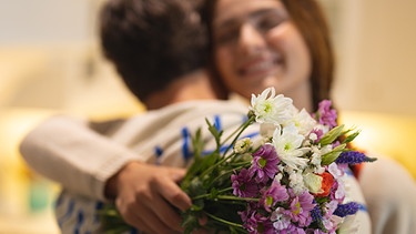 Freude! Ein junger Mann gibt einer jungen Frau einen Blumenstrauß und umarmt sie.
| Bild: stock.adobe.com