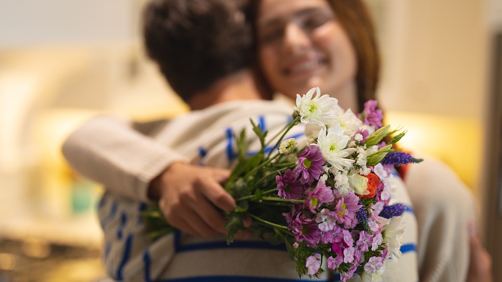 Freude! Ein junger Mann gibt einer jungen Frau einen Blumenstrauß und umarmt sie.
| Bild: stock.adobe.com