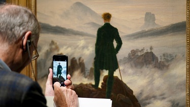 Ein Mann fotografiert das Werk "Wanderer über dem Nebelmeer" von Caspar David Friedrich in der Hamburger Kunsthalle. Im Jubiläumsjahr zum 250. Geburtstag von Caspar David Friedrich (1774-1840) gibt es dort eine große Retrospektive zu sehen. | Bild: dpa-Bildfunk/Marcus Brandt