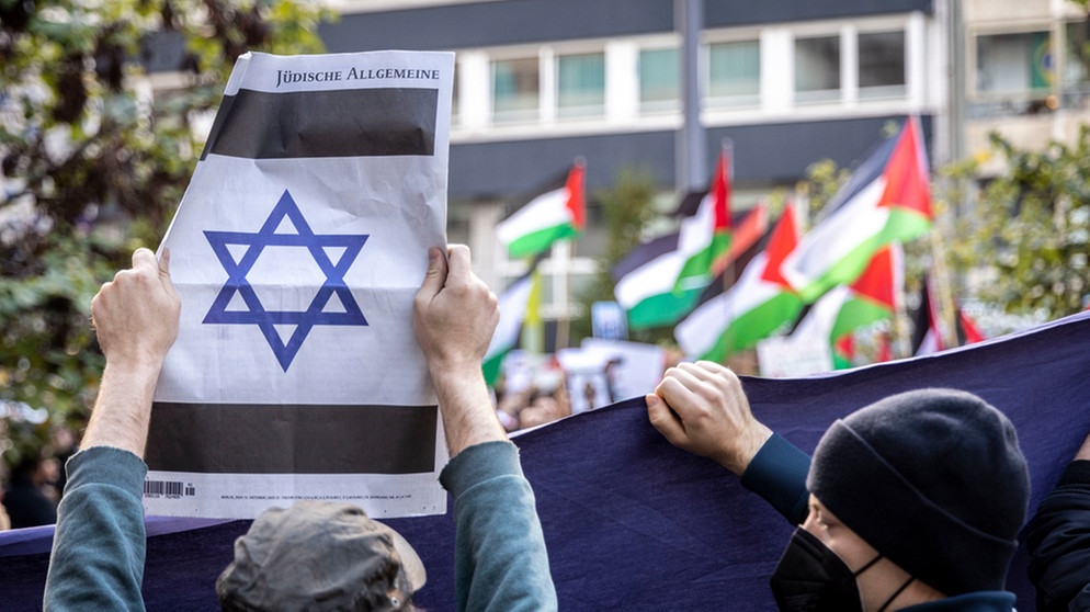 Pro-Israelischer Gegendemonstrant zeigt eine jüdische Zeitung mit einem Davidstern, im Hintergrund Pro-Palästinensische Demonstranten (Veranstaltung im Düsseldorf am 14. Oktober 2023) | Bild: picture-alliance/dpa