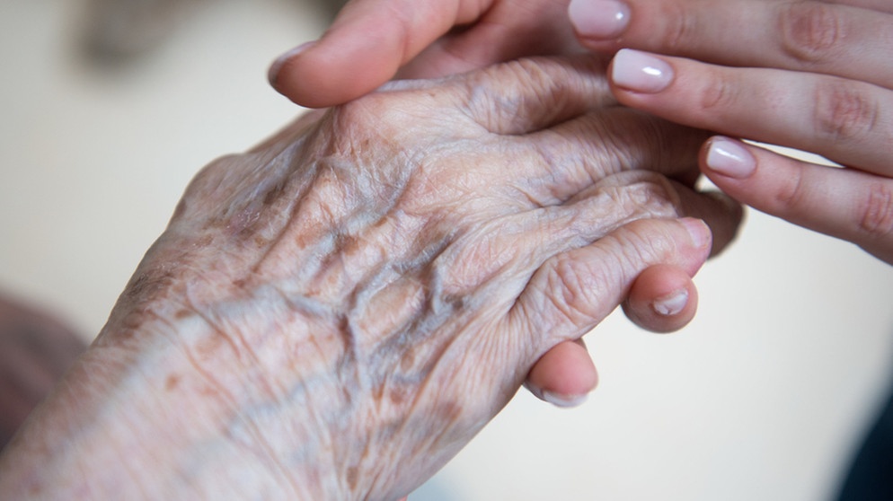 Eine pflegende Person hält die Hände einer pflegebedürftigen Person.  | Bild: dpa-Bildfunk/Christophe Gateau