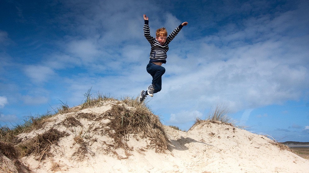 Kind springt von einer Sanddüne | Bild: picture alliance / blickwinkel/AGAMI/B. Haasnoot | AGAMI/B. Haasnoot