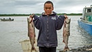 Ein Junge in Alaska, der zu der Gruppe der Yup’ik gehört, hält gefangene Fische hoch. | Bild: BR / Dirk Rohrbach