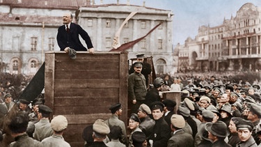 Lenin spricht auf dem Swerdlow-Platz in Moskau zu Soldaten der Roten Armee; rechts auf den Stufen der Tribüne stehend: Leo Trotzkij (vorn) und Lew Kamenew. (Nachdem Trotzki und Kamenew unter Stalin in Ungnade gefallen waren, wurde ab den 30er Jahren nur noch das linke Bilddrittel verwendet. | Bild: picture alliance / akg-images